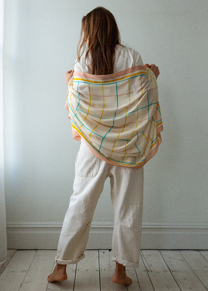 Person holding a colorful checkered scarf in a minimalistic room.