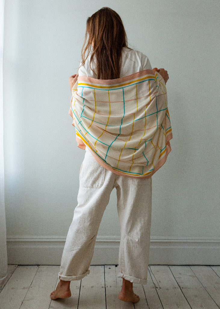 Person holding a colorful checkered scarf in a minimalistic room.