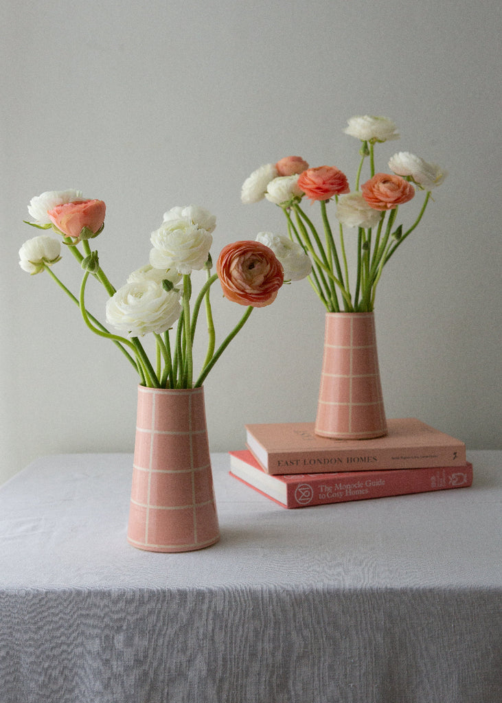 Two pink vases with flowers on a white surface and gray background