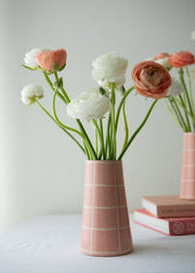Pink vase with flowers on a white surface