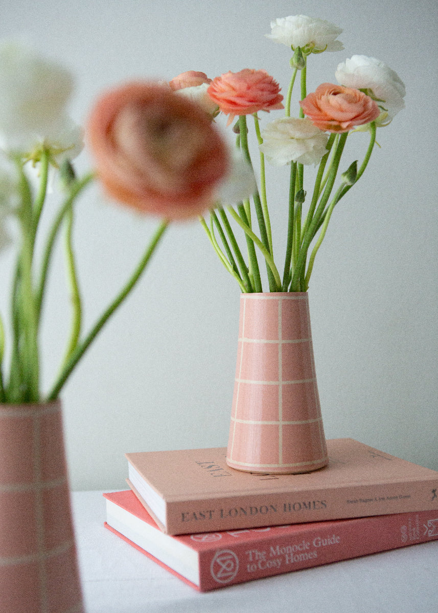 Pink vases with flowers on books against a light background