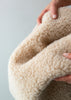 Close-up of a hand holding a beige textured fabric against a gray background