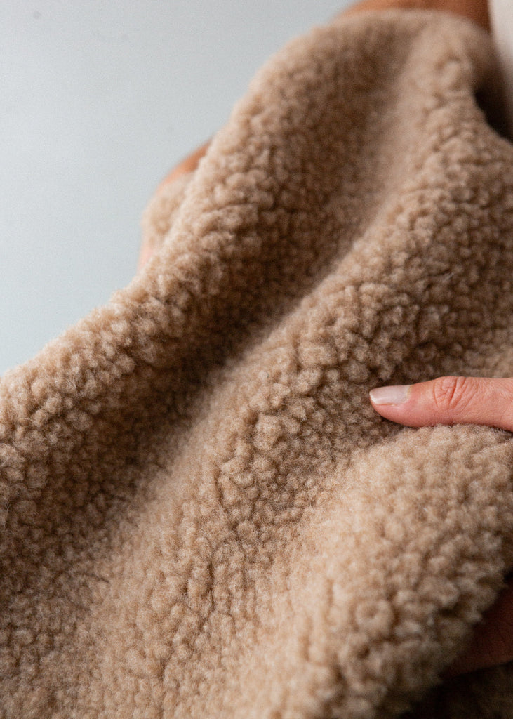 Close-up of a person holding a beige fleece blanket against a neutral background