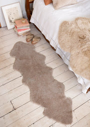 Double oatmeal shearling rug on floor next to a bed