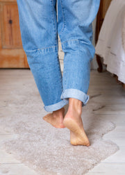 Person wearing blue jeans walking on a textured rug indoors.