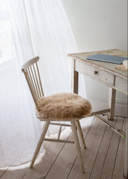 Wooden chair with a fur seat pad next to a wooden desk in a softly lit room.