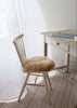 Wooden chair with a fur seat pad next to a wooden desk in a softly lit room.