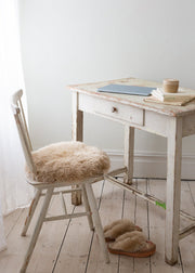 Small wooden desk with a chair with s sheepskin seat pad in a room with white walls and wooden floor.