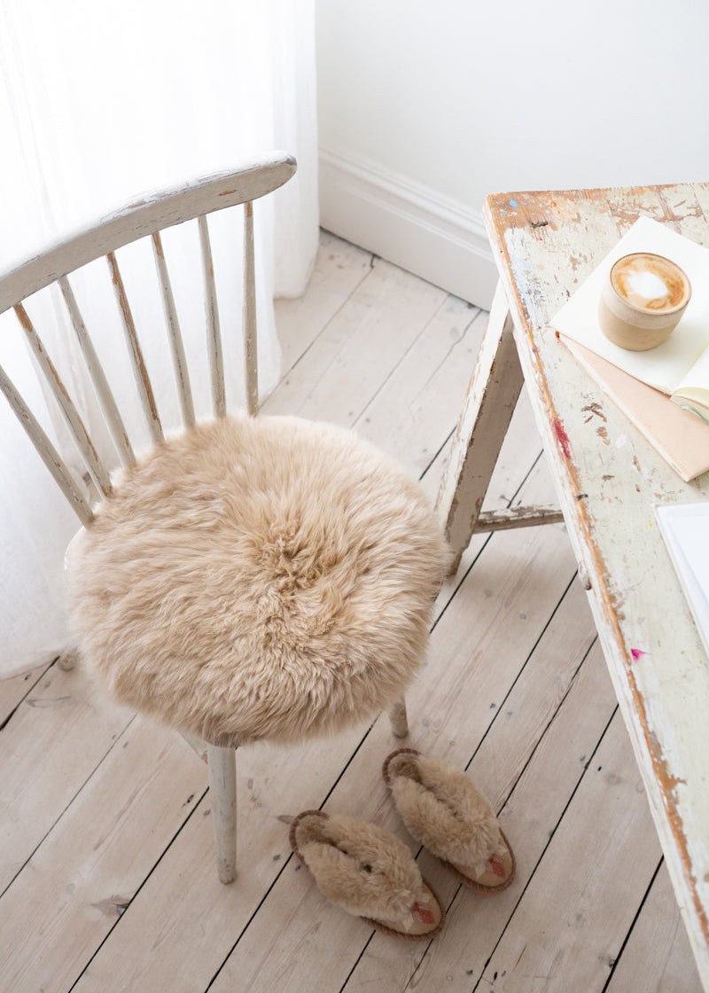 Chair with a fluffy sheepskin seat cushion on a wooden floor next to a table with a candle.