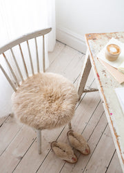 Chair with a fluffy sheepskin seat cushion on a wooden floor next to a table with a candle.