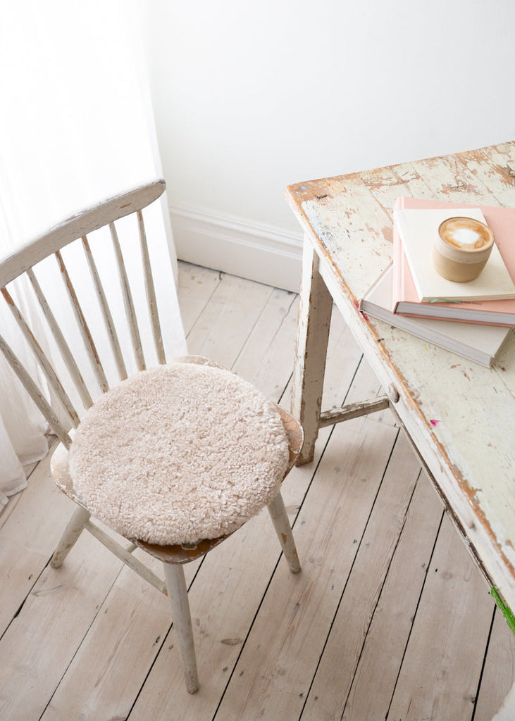 Chair with a textured cushion on a wooden floor next to a small table with books and a candle.