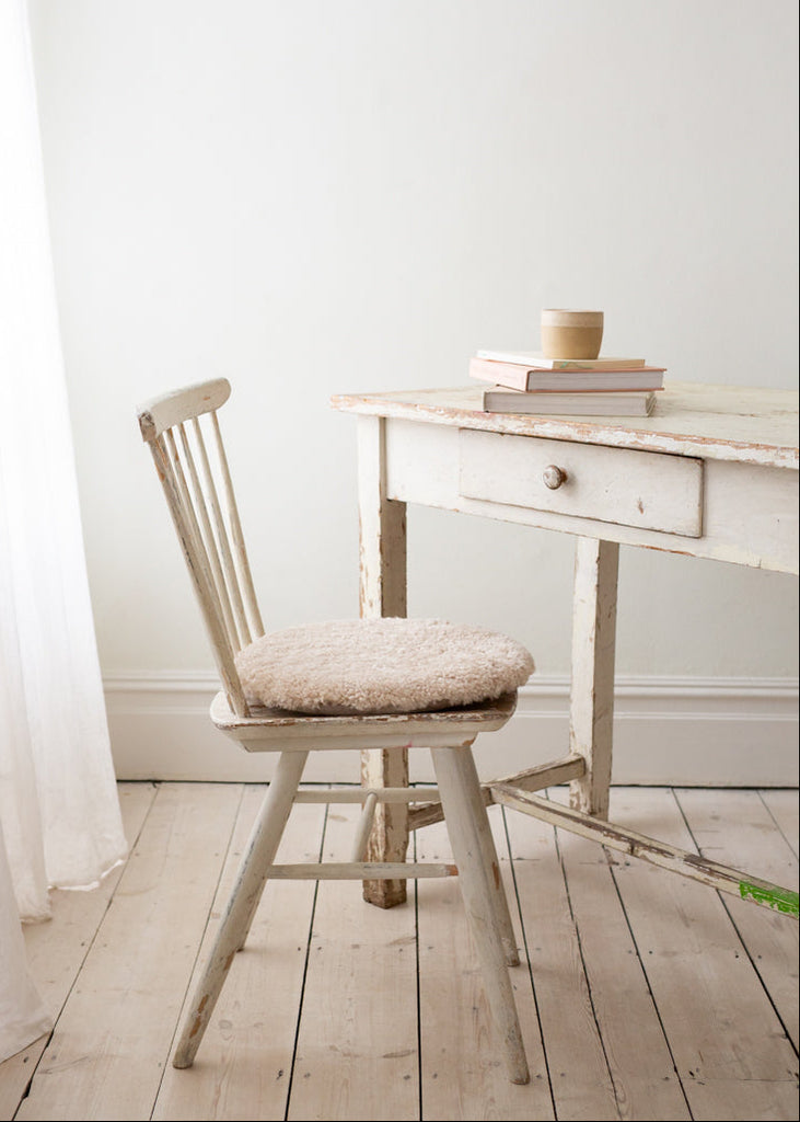 Wooden chair with a cushion in front of a white desk in a room with light wood flooring and white walls.