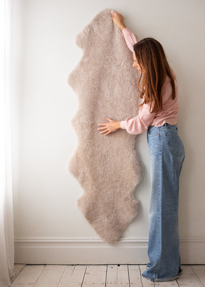 Woman holding a sheepskin rug against a white wall