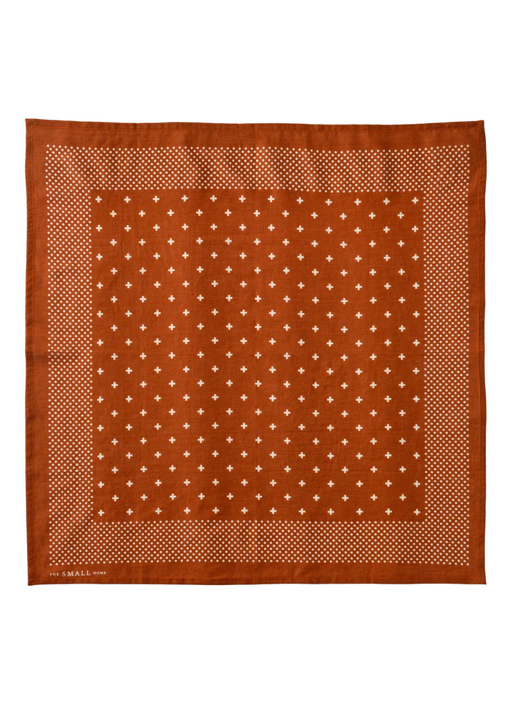 A square terracotta orange silk scarf with a white geometric pattern, featuring a central field of small white diamond motifs and a dotted border, shown flat against a white background.