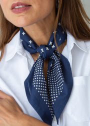 A navy blue silk scarf with white cross and dot patterns, tied around the neck of a woman wearing a white collared shirt.