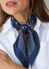A navy blue silk scarf with white cross and dot patterns, tied around the neck of a woman wearing a white collared shirt.
