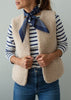 A woman wearing a cream sherpa fleece vest over a navy and white striped long-sleeve shirt, accessorized with a navy blue patterned neck scarf and blue jeans.