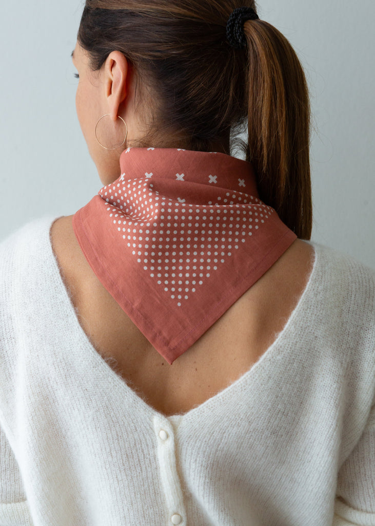 A woman shown from the back wearing a dusty rose bandana with white polka dots and small white cross motifs, styled over her shoulders.