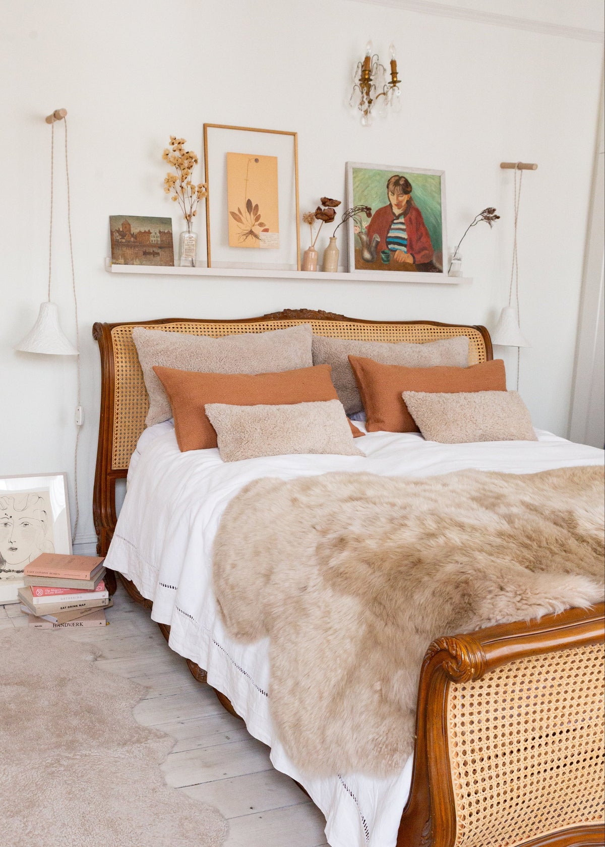 Neatly made bed with sheepskin cushions and rugswith wooden headboard in a bright bedroom.